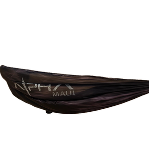 A black hammock called "The Sky Sleeper" prominently displays the text "Alpha Maui" alongside a logo that features a stylized wave and a star. The hammock is fully stretched out, clearly showcasing the text and design, with no background elements included so that only the hammock is in view.