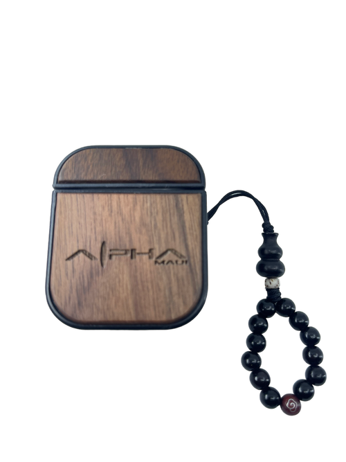An Alpha Airpod Case made from wood, featuring the engraved text "Alpha Male," accompanied by a dark beaded bracelet strung together. The case boasts a smooth finish and sleek, compact design perfect for your beach apparel. The bracelet showcases spherical black beads accented with a single bead adorned with a red and white spiral design.