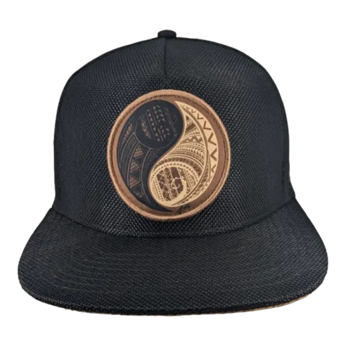 A black cap featuring a circular patch on the front. The patch displays a yin-yang symbol with intricate geometric patterns in black and brown. The background of the cap is a textured fabric.
