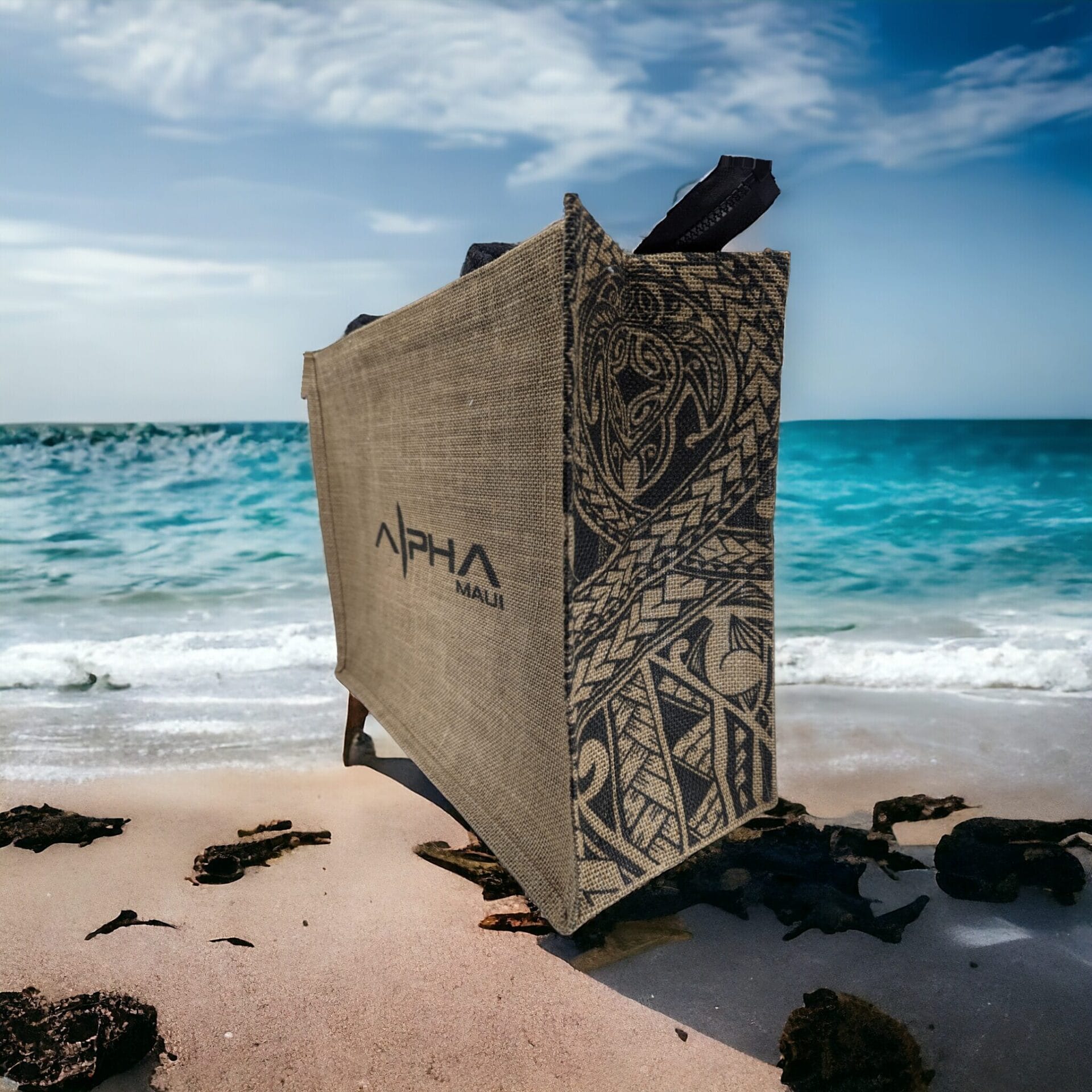 A large, intricately designed kiteboard with tribal patterns rests against a sandy beach. The ocean waves gently lap the shore under a clear blue sky.