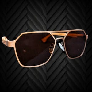 A pair of modern, geometric-shaped sunglasses with dark lenses and a metallic frame, displayed against a textured black chevron-patterned background.